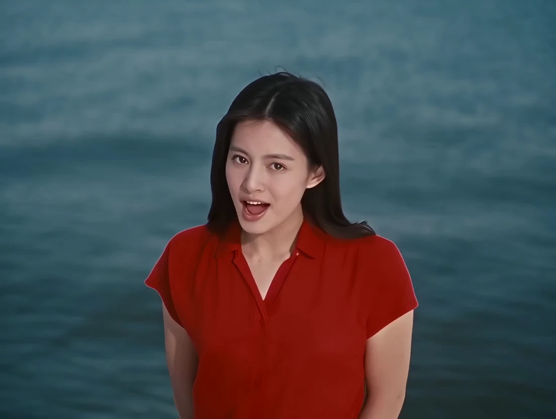 A woman with long black hair in a red top sings by the sea