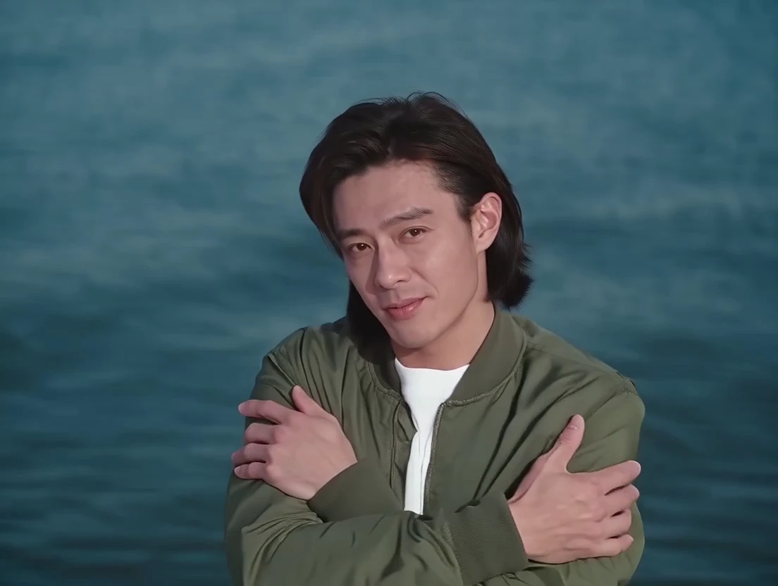 The singer hugs his arms as he sings by the water